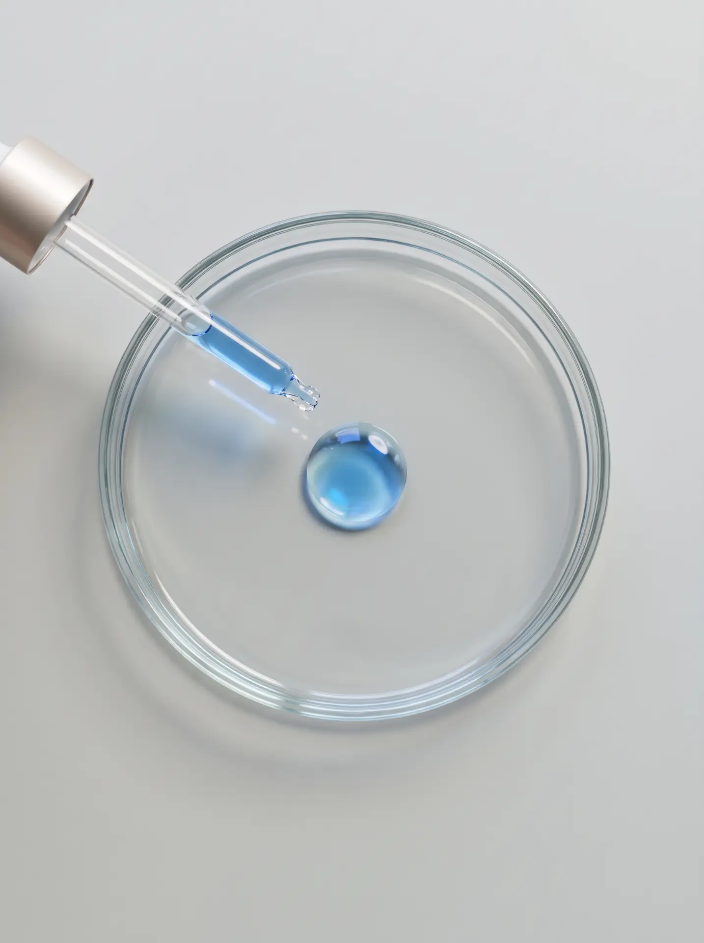 A dropper releasing a blue serum drop into a glass dish